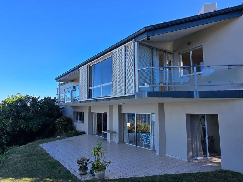 Rear view of the multi-level house featuring a tiled patio, glass balustrades, sliding doors, and elevated balcony with ocean views.