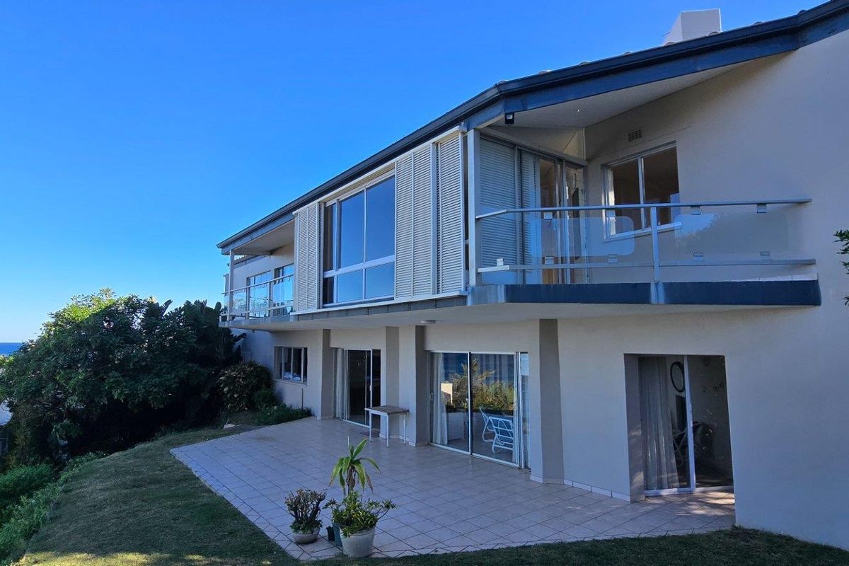 Rear view of the multi-level house featuring a tiled patio, glass balustrades, sliding doors, and elevated balcony with ocean views.