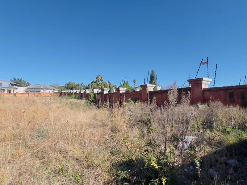 A vacant residential plot featuring an extensive perimeter boundary wall with integrated electric fencing and concrete pillars.