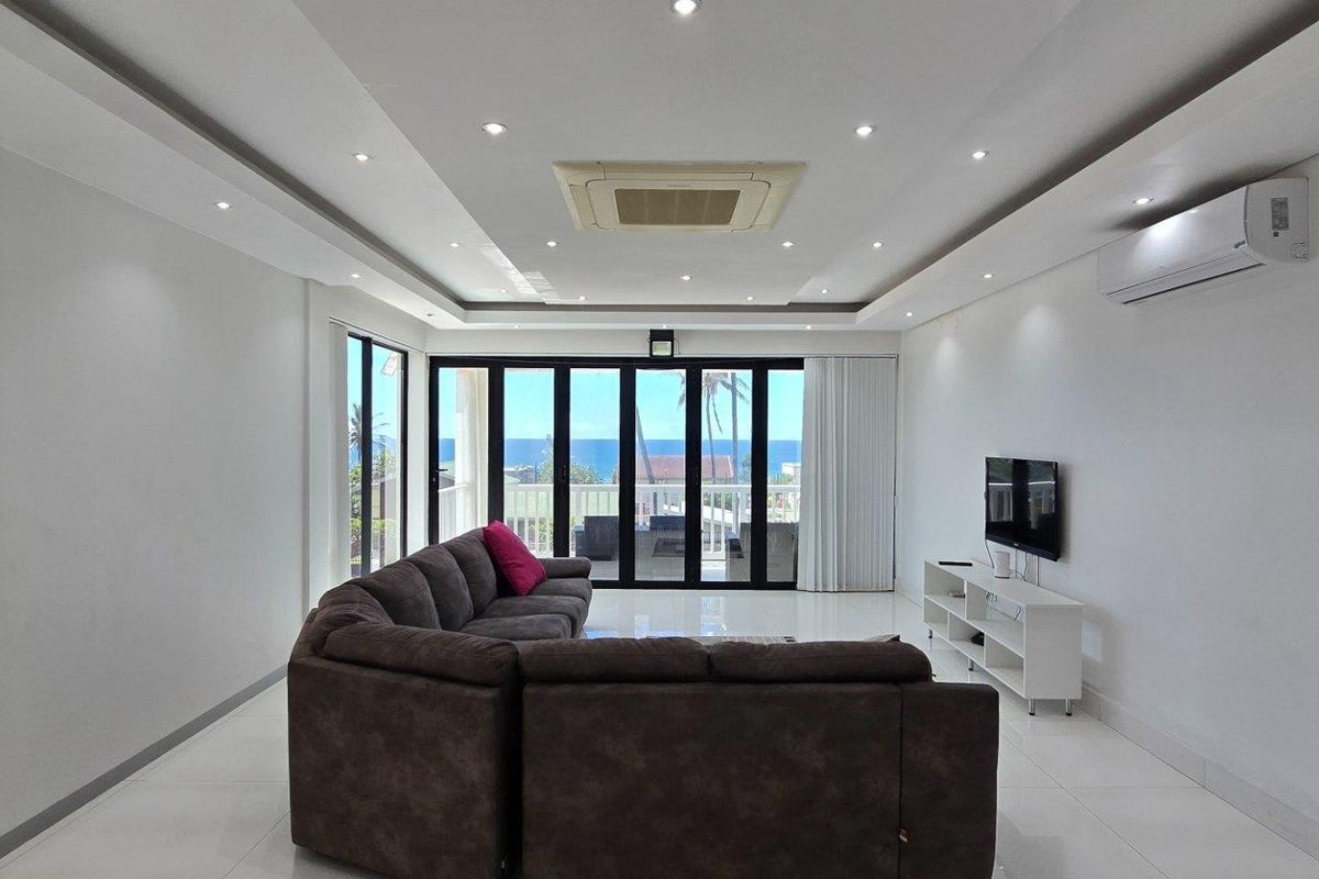 Spacious living room featuring recessed ceiling lighting, ducted air conditioning, tiled flooring, and large glass sliding doors opening to a scenic balcony.