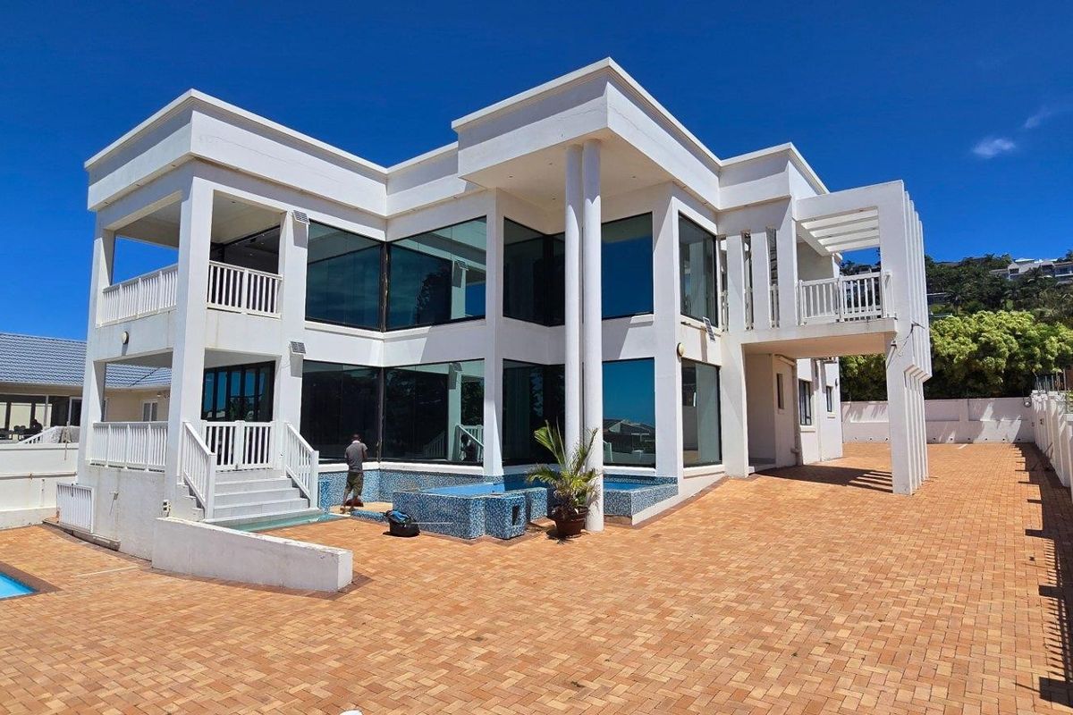A modern multi-story residential property featuring large glass windows, a paved courtyard, and a swimming pool.