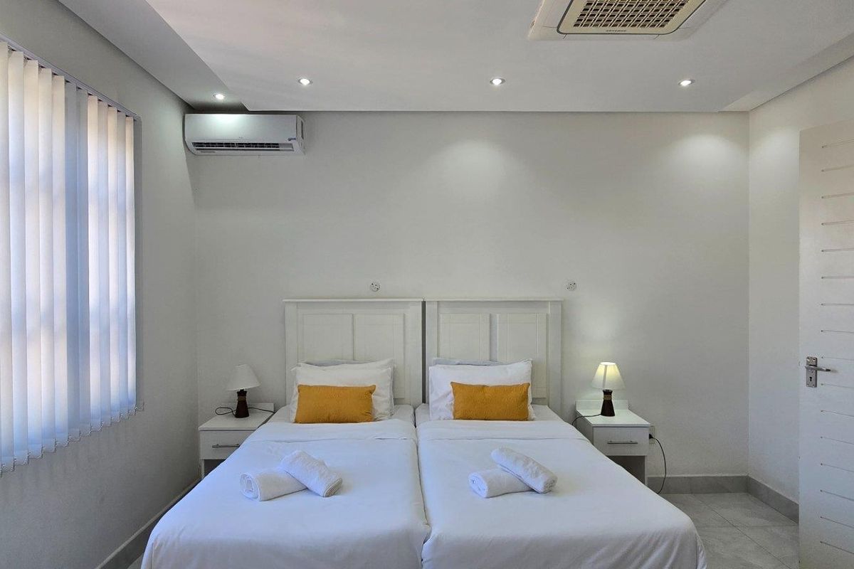 A clean and well-maintained bedroom featuring recessed ceiling lighting, a wall-mounted air conditioning unit, and vertical window blinds.