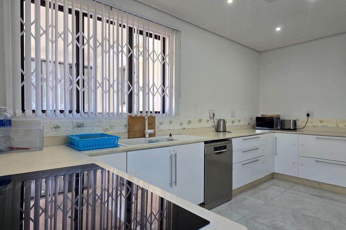 Modern kitchen featuring white cabinetry, stone countertops, integrated dishwasher, and a built-in induction hob, complemented by tiled flooring and security window shutters.