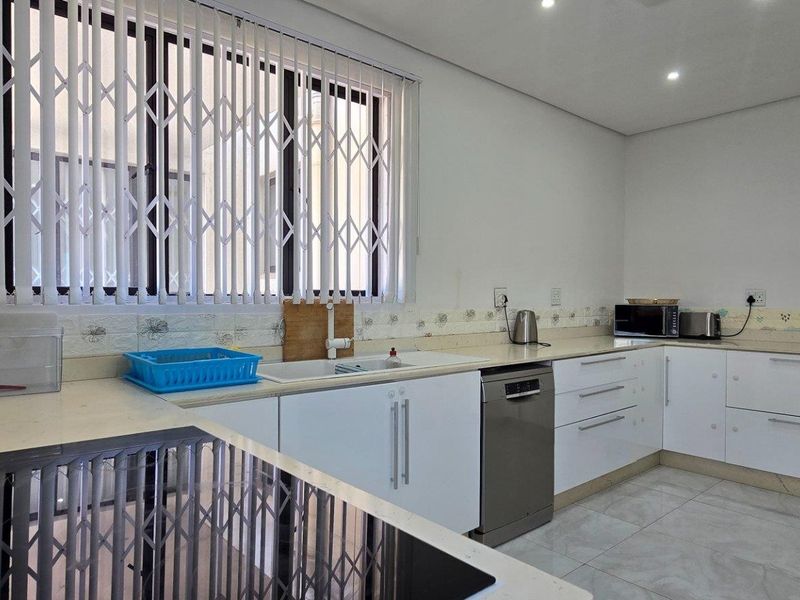 Modern kitchen featuring white cabinetry, stone countertops, integrated dishwasher, and a built-in induction hob, complemented by tiled flooring and security window shutters.