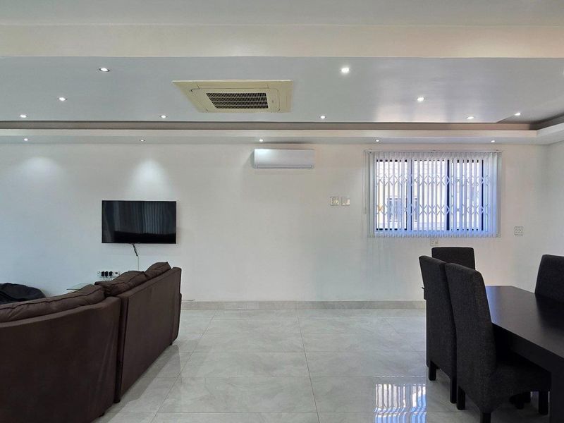 Spacious open-plan living and dining area featuring recessed ceiling lighting, a central air conditioning unit, and large format floor tiles.