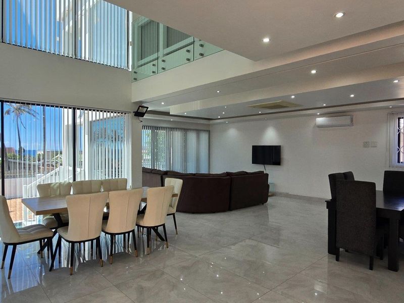 Spacious open-plan living and dining area featuring double-volume ceilings, large glass sliding doors, polished floor tiles, and recessed downlighting.