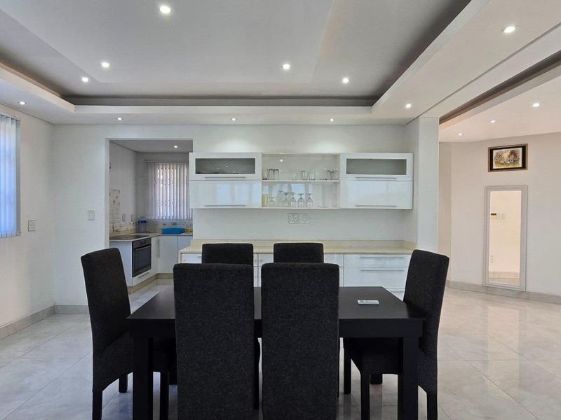 Open plan dining area featuring modern recessed ceiling lighting, tiled flooring, and a view into the adjacent kitchen with built-in cabinetry.
