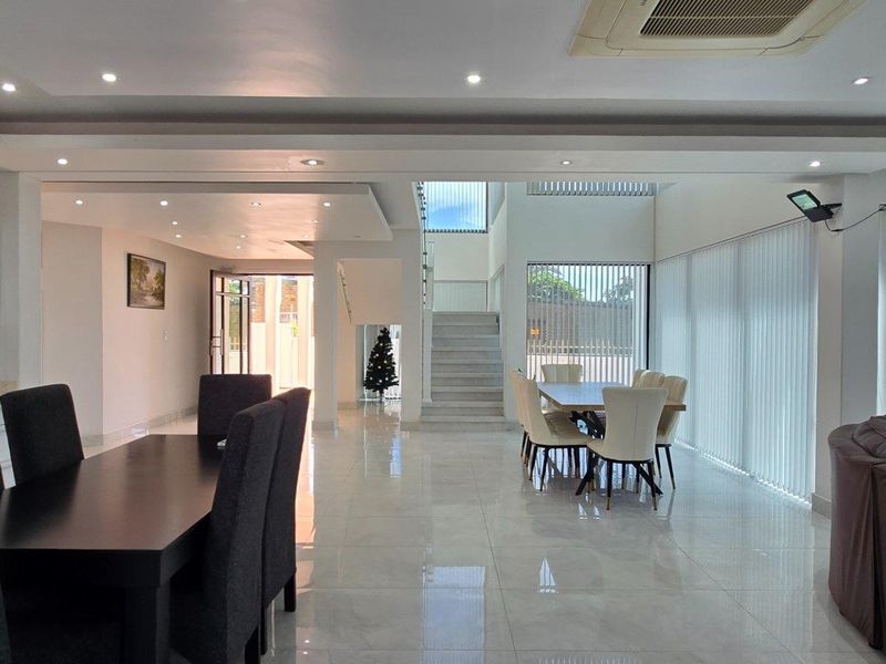 Spacious open-plan living and dining area featuring polished tile flooring, recessed ceiling lighting, and a central staircase leading to the upper level.