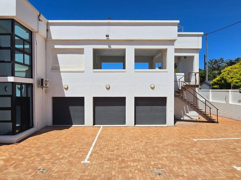 Exterior view of a multi-car garage facility with paved driveway, external staircase, and upper-level balcony area.