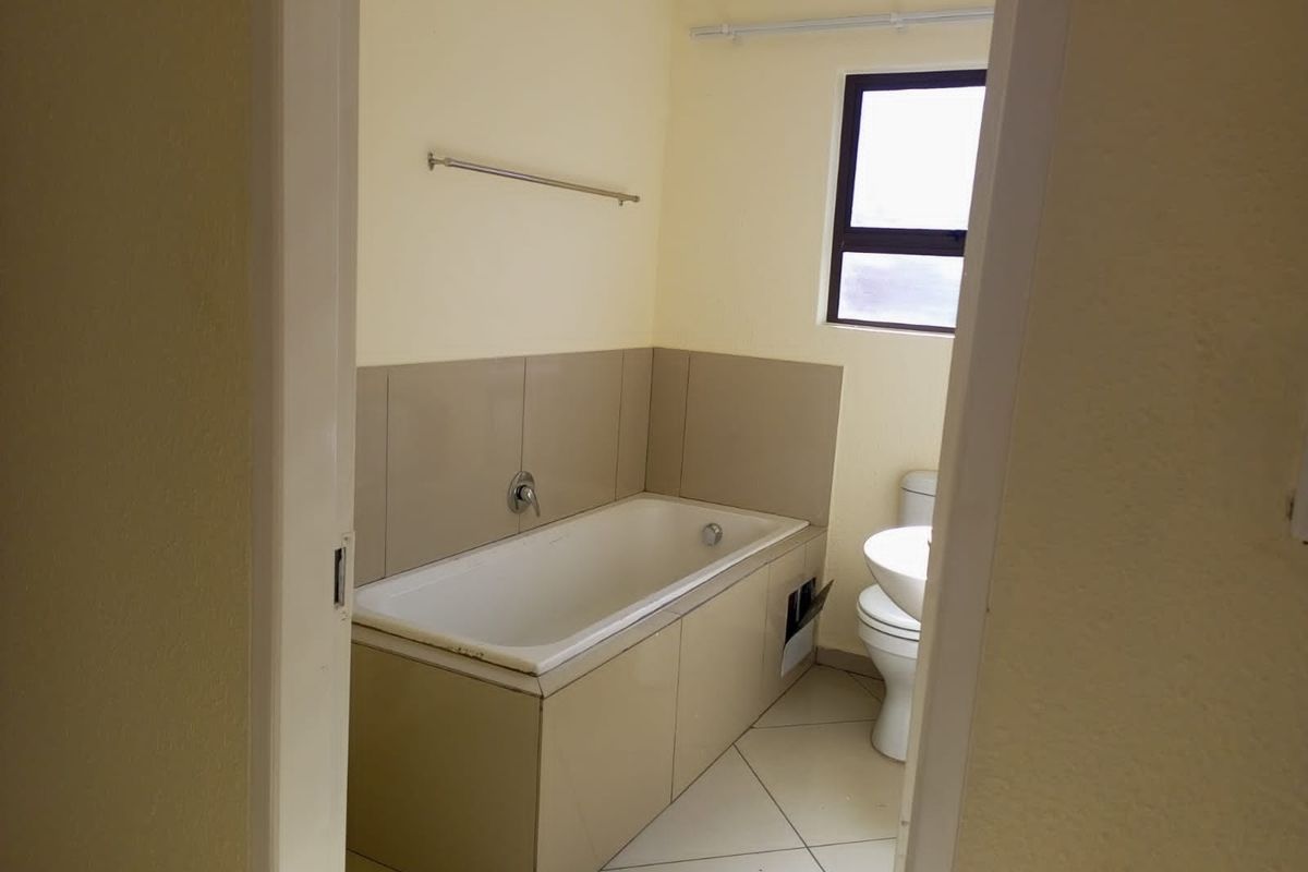 A functional bathroom featuring a built-in bathtub with tiled surround, a toilet, and a window providing natural light.