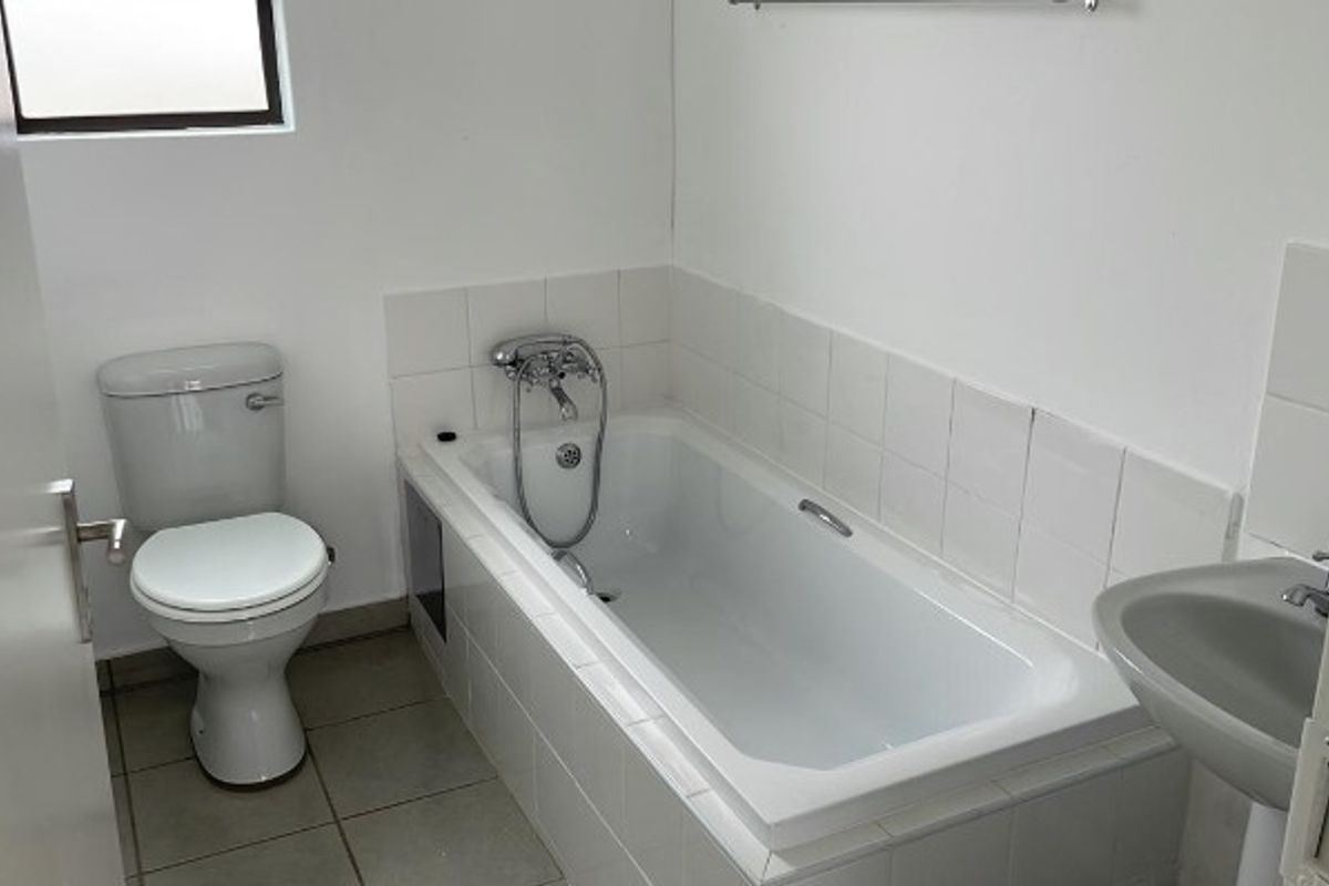 A functional bathroom featuring a standard bathtub with shower mixer, a pedestal basin, and a toilet, finished with white wall tiles.