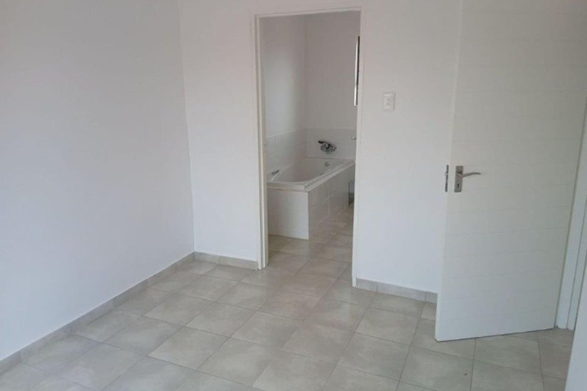 A view from a bedroom into an en-suite bathroom featuring tiled flooring and a built-in bathtub.