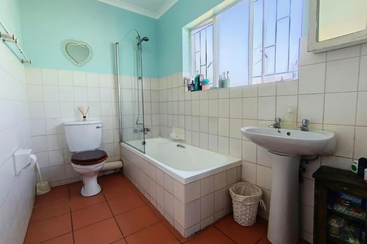 A functional bathroom featuring a bathtub with a glass shower screen, a pedestal basin, and a toilet, finished with tiled walls and flooring.