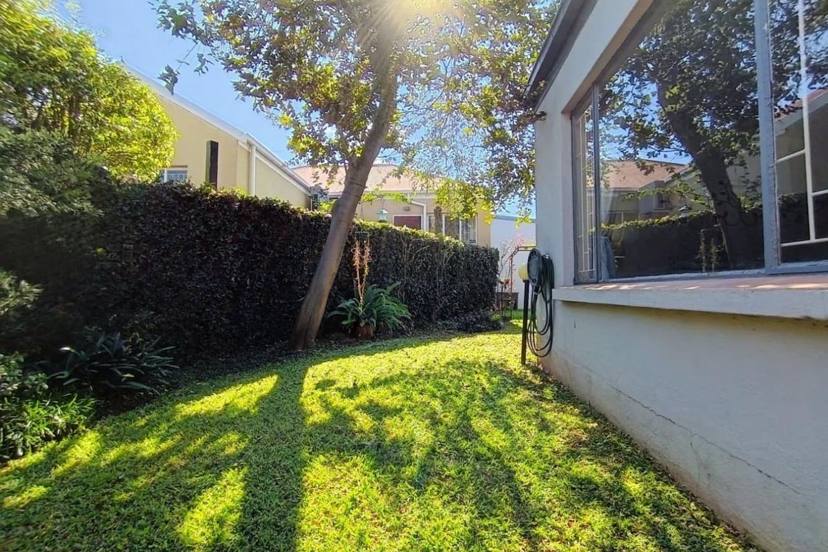 A private rear garden area featuring a manicured lawn, established hedge boundary, and direct access to the side of the townhouse structure.