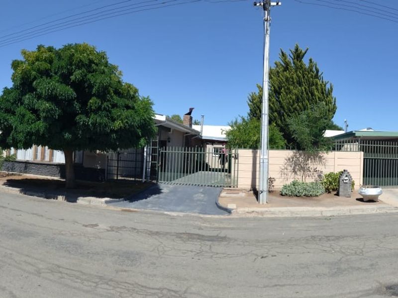 A wide-angle street view of the property featuring a gated entrance, paved driveway, and perimeter walling in a residential neighbourhood.