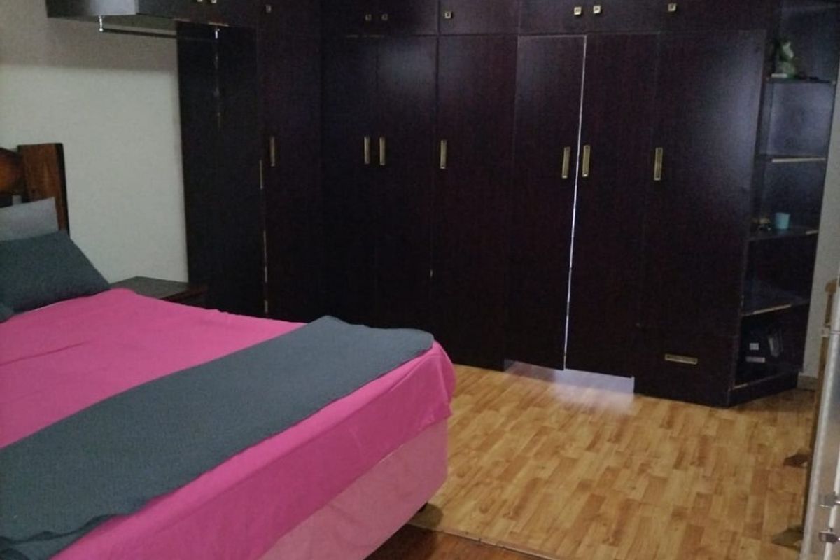 A bedroom featuring extensive dark wood built-in cabinetry, polished wooden flooring, and a ceiling-mounted light fixture.
