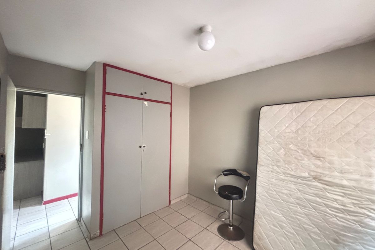 A bedroom featuring built-in wardrobe storage, tiled flooring, and a simple overhead light fixture, with an adjacent view into a secondary room.