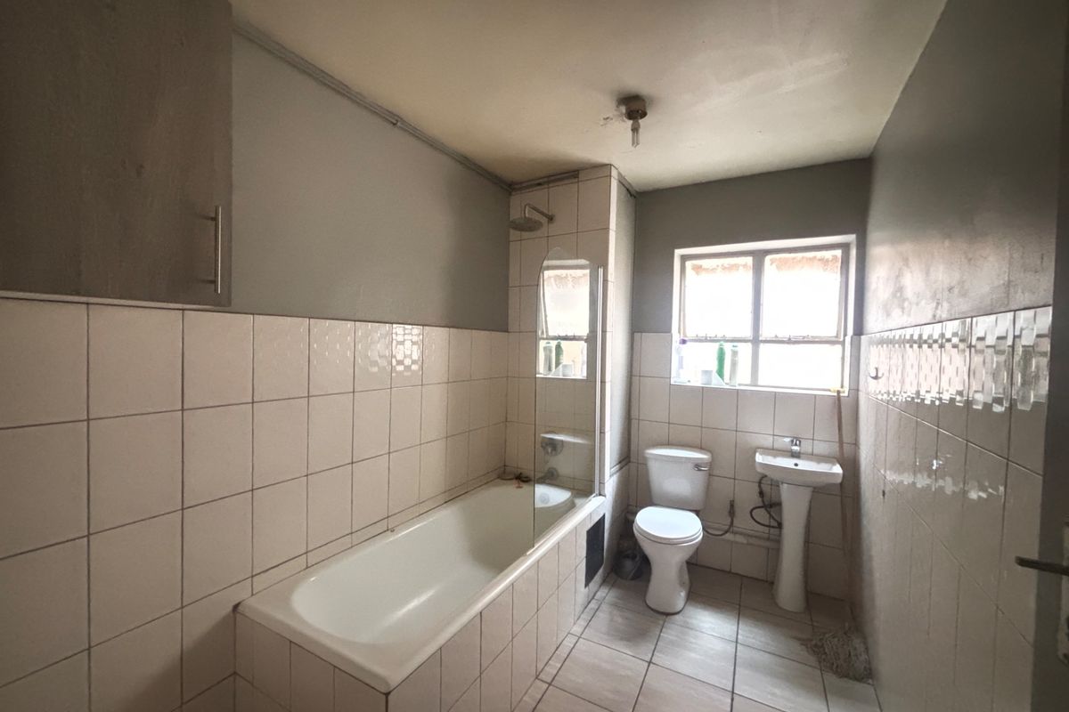 A dated bathroom featuring a built-in bathtub with a glass screen, a pedestal basin, and a toilet, requiring cosmetic updates and maintenance.