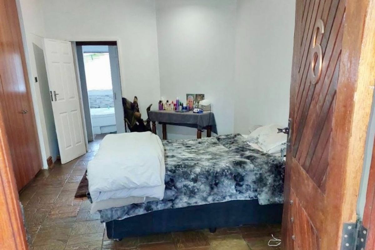 A bedroom featuring stone tile flooring, timber crown molding, and a built-in cupboard, with an adjoining bathroom visible through the doorway.