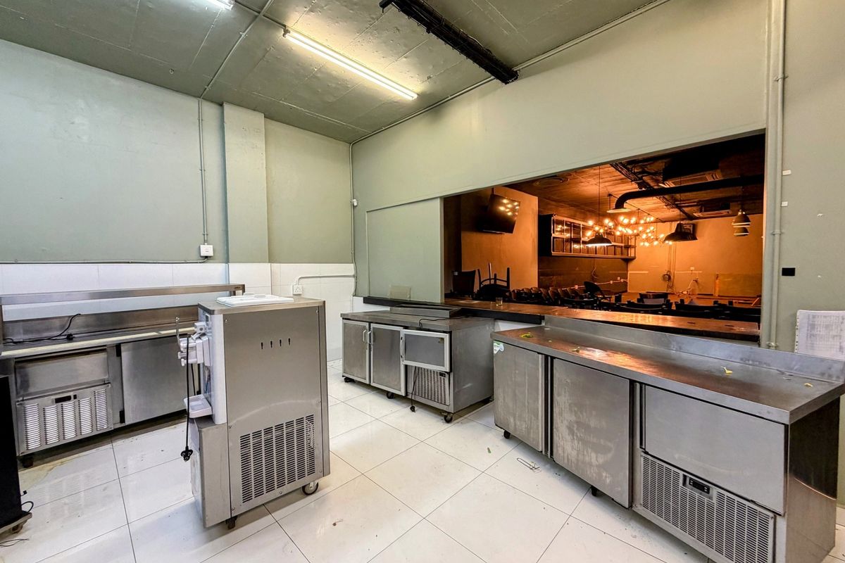 Commercial kitchen area featuring stainless steel prep counters, under-counter refrigeration units, and a service pass-through window connecting to the main office space.