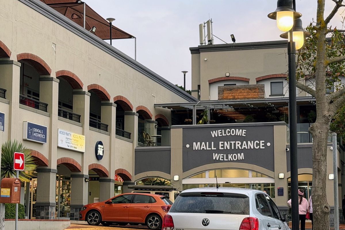 Front exterior view of a commercial office and retail mall entrance featuring arched architectural details and paved access area.