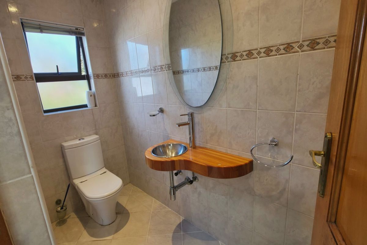 A compact bathroom featuring floor-to-ceiling wall tiles, a modern vessel sink set into a wooden vanity shelf, and a wall-mounted toilet.