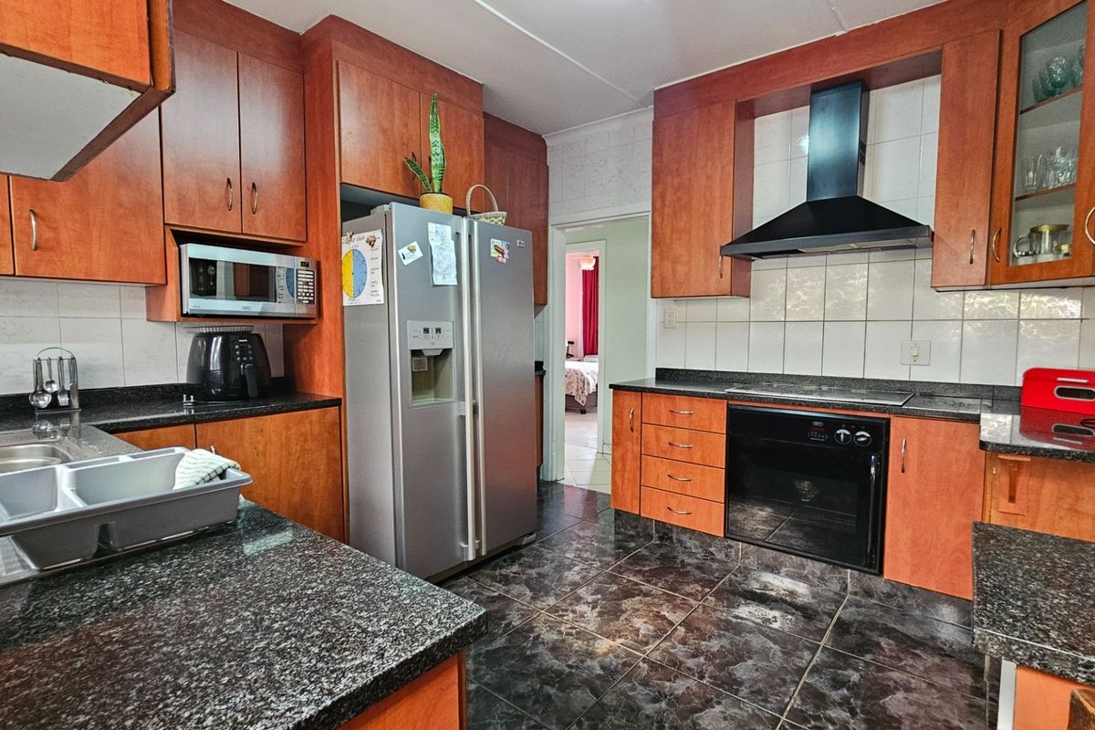 A functional kitchen featuring wood-toned cabinetry, granite countertops, a built-in oven, and a black extractor fan with tiled backsplash.
