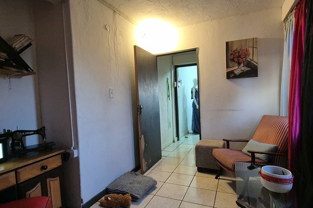 A living area featuring tiled flooring and a doorway leading to an adjacent room, showing signs of wear and dated finishes.