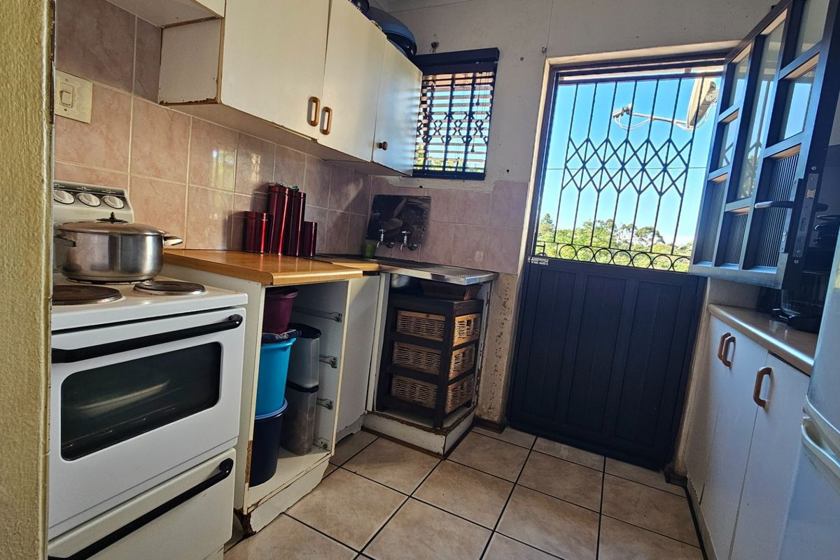 Compact kitchen featuring tiled flooring, built-in cabinetry, and a freestanding stove, with direct access to the exterior via a security gate.