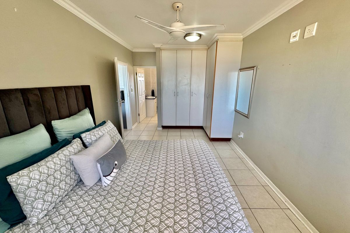A bedroom featuring built-in wardrobes, tiled flooring, a ceiling fan, and an en-suite bathroom access.