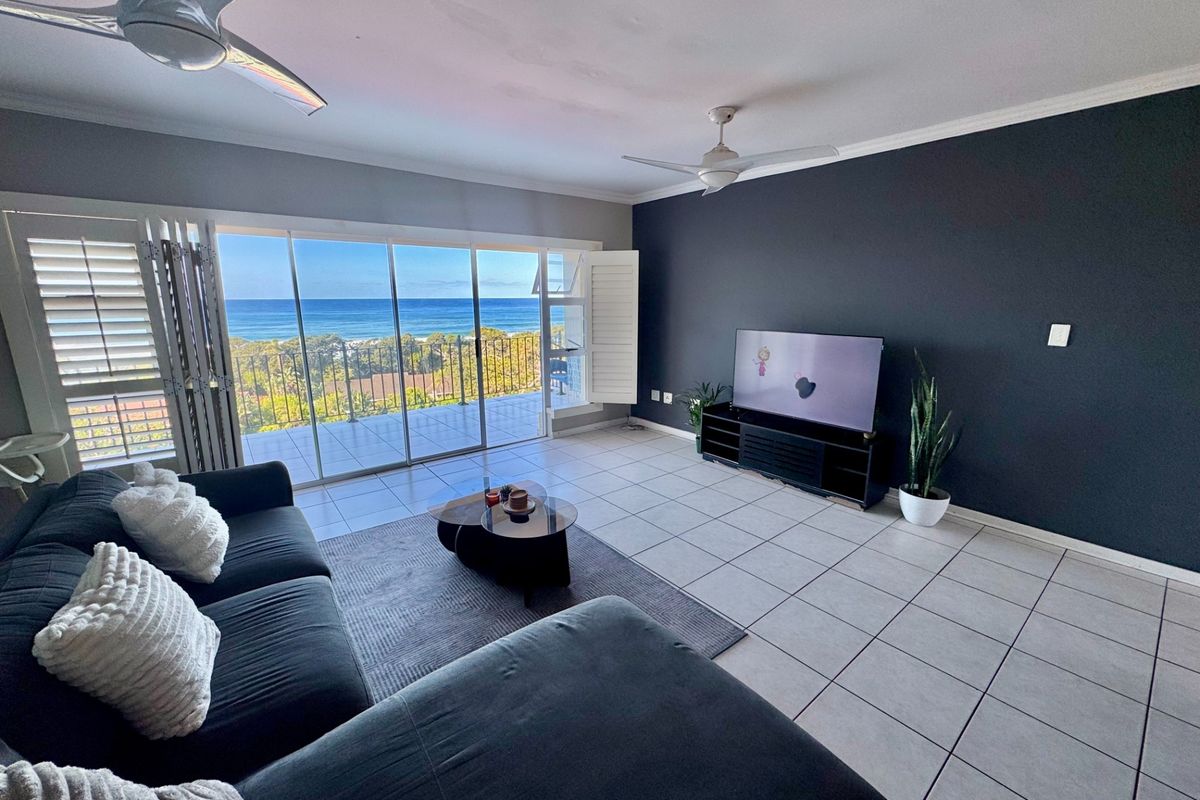 Spacious living room featuring large sliding glass doors that open to a balcony with panoramic ocean views and tiled flooring throughout.