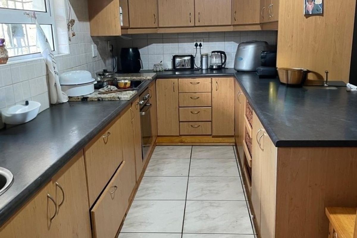 A functional galley-style kitchen featuring wood-finish cabinetry, dark laminate countertops, and tiled flooring with a built-in oven and hob.