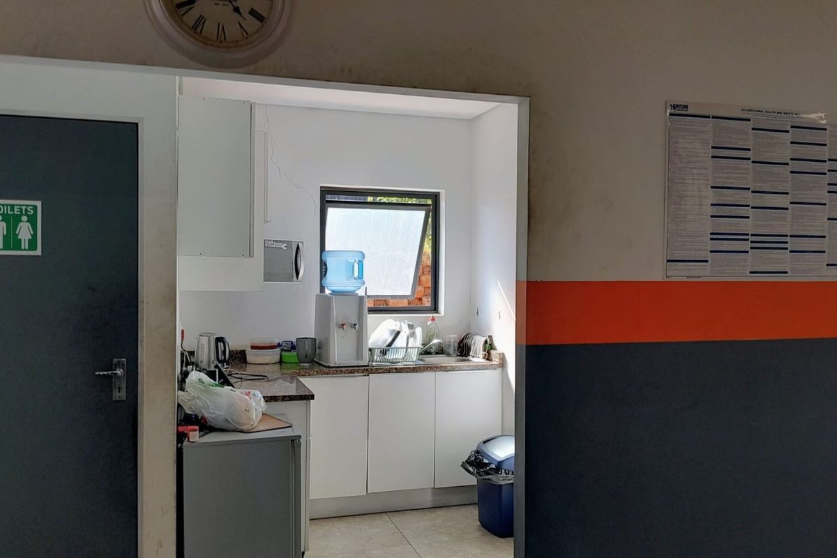 A compact commercial kitchenette featuring built-in cabinetry, a granite countertop, and a sink, adjacent to a designated restroom area.