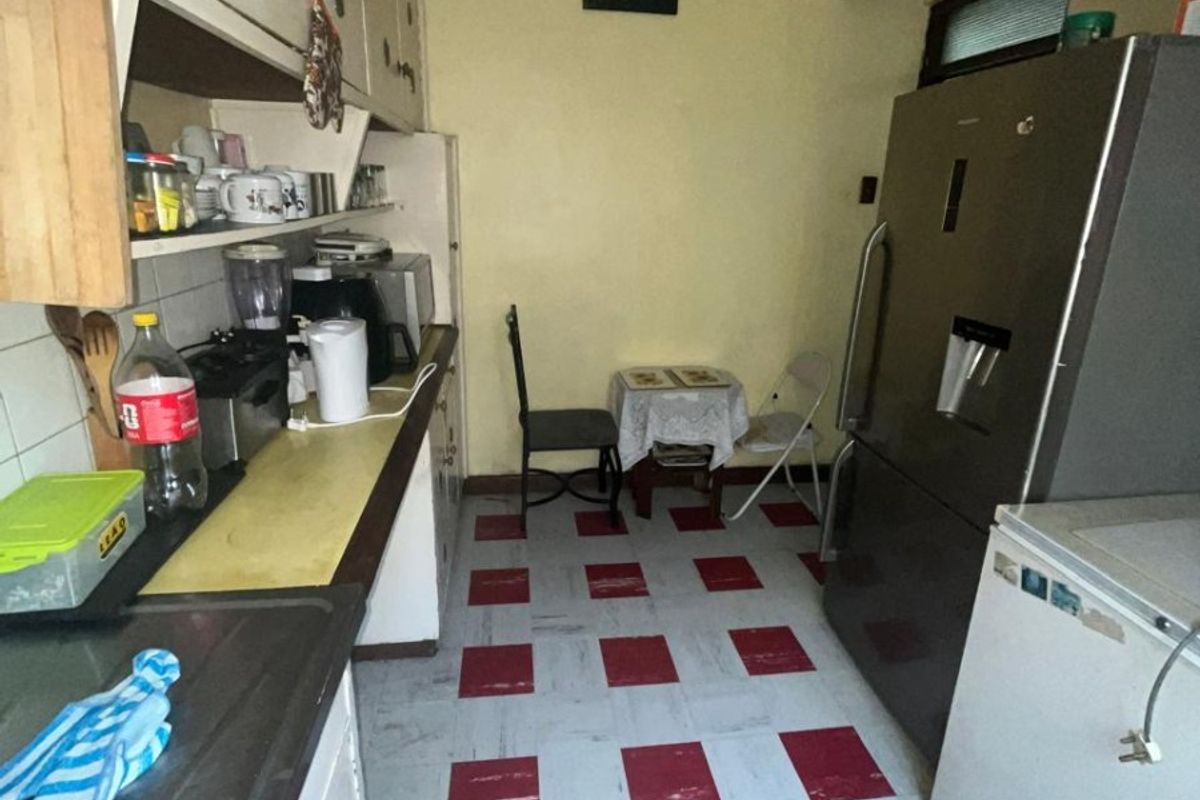 A compact kitchen featuring dated cabinetry, a stainless steel sink, and distinctive red and white checkered floor tiles.