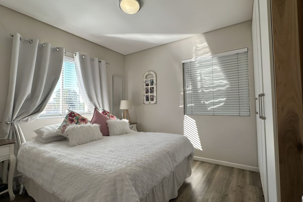 A well-lit bedroom featuring built-in wardrobes, wood-look flooring, and dual window treatments, providing a comfortable and functional living space.