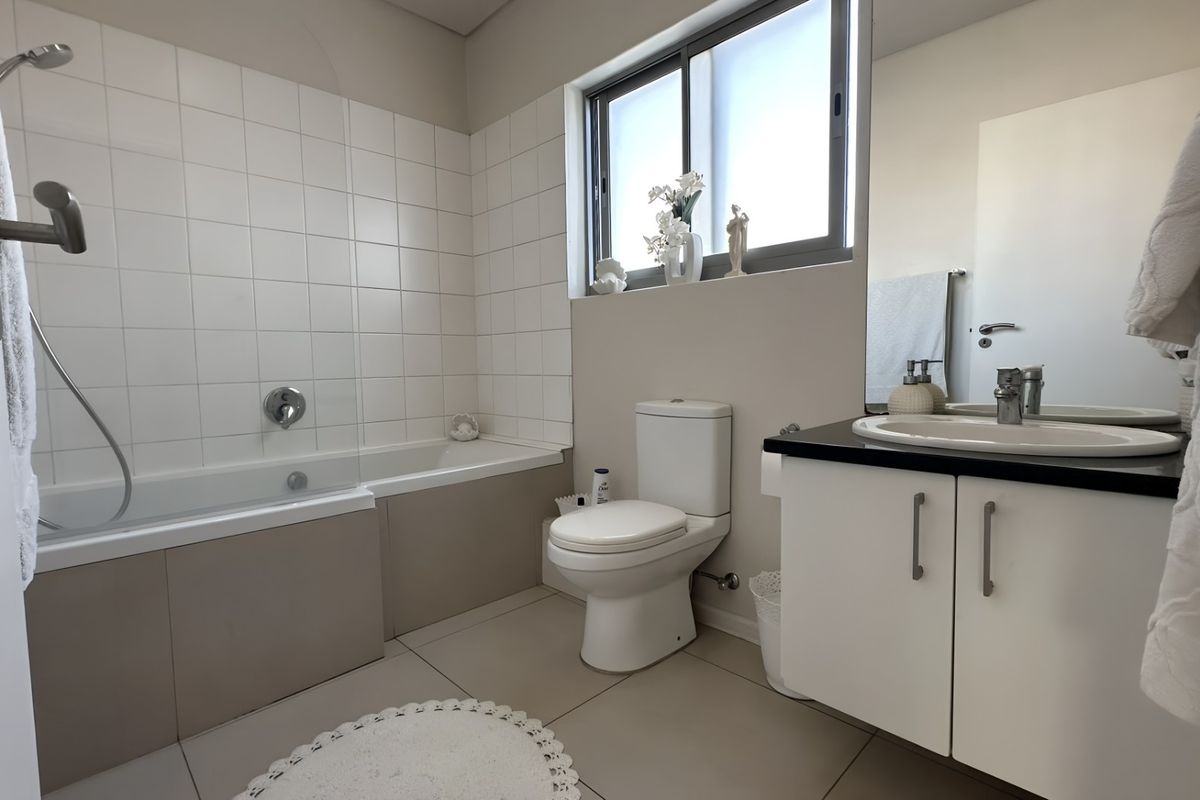 A functional bathroom featuring a built-in bathtub with shower mixer, a white toilet, and a vanity cabinet with a countertop basin.