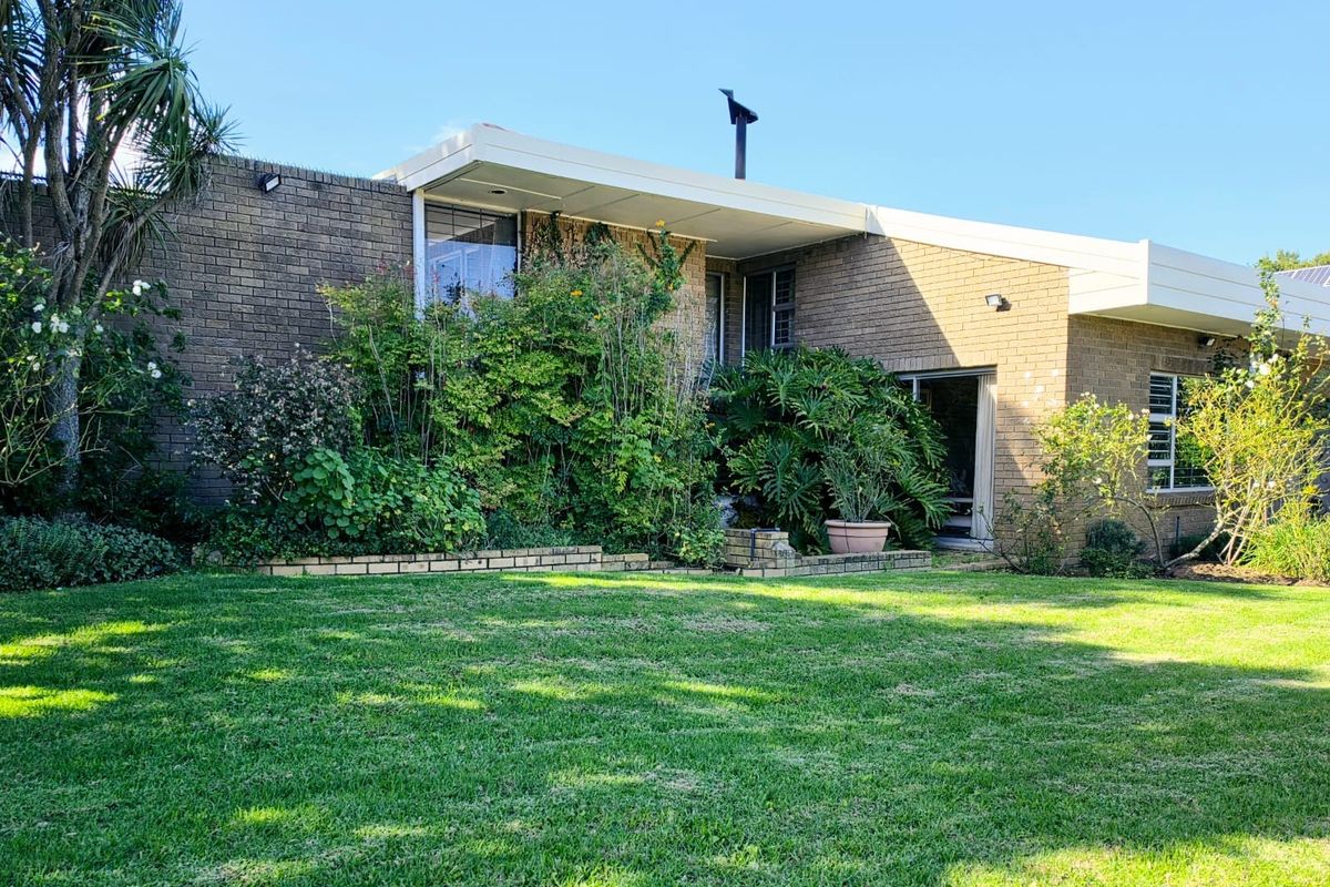 Rear view of a brick-clad house featuring a flat roofline, large windows, and direct access to a spacious lawn and garden area.