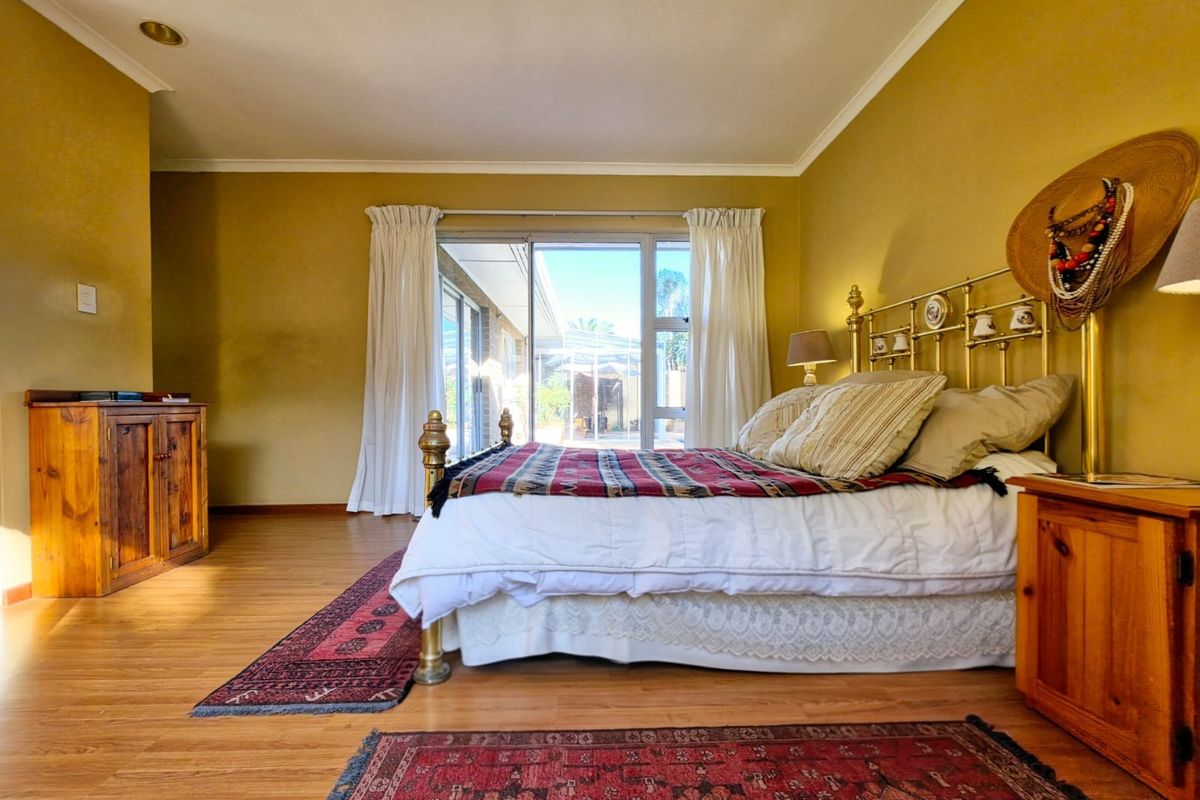 A spacious bedroom featuring laminate flooring, mustard-toned walls, and sliding glass doors that provide direct access to an outdoor patio area.