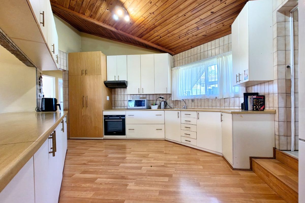 A spacious kitchen featuring white cabinetry, wood-look laminate flooring, and a distinctive vaulted timber-paneled ceiling with integrated oven and extractor fan.