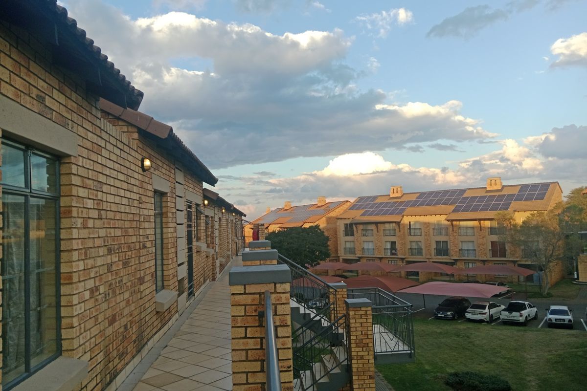 An elevated view of an apartment complex exterior featuring brick facade, tiled walkways, and solar panel installations on the roof.