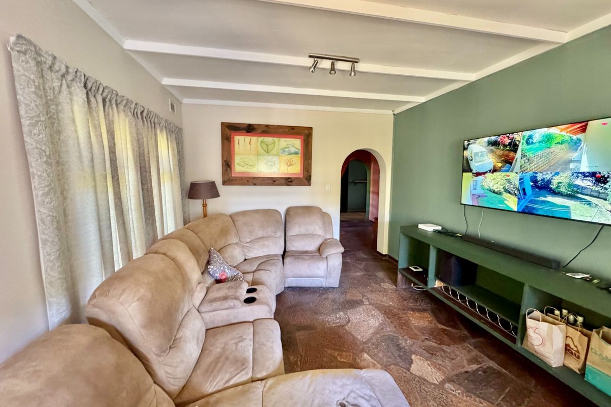 Living room featuring exposed beam ceilings, natural stone flooring, and a built-in media console with an arched doorway leading to adjacent spaces.