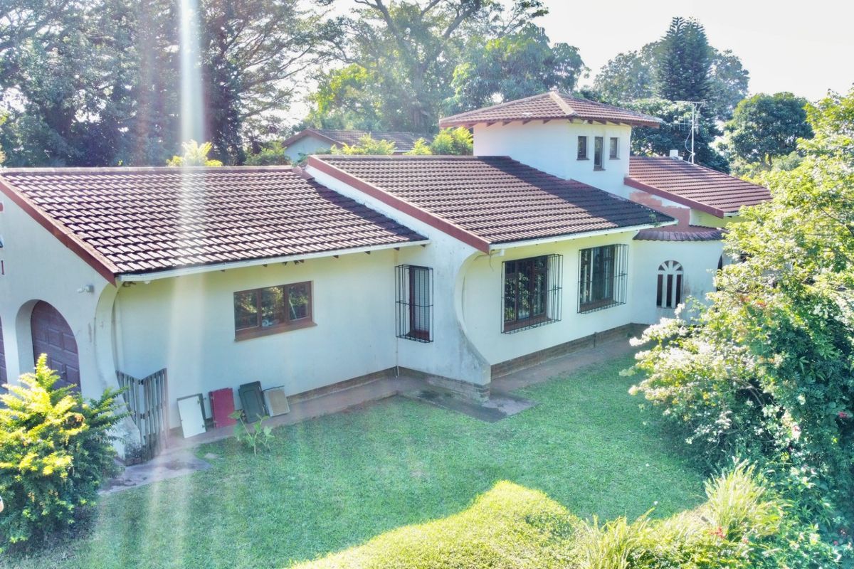 An elevated view of the rear exterior of a house featuring a tiled roof, a turret-style architectural element, and a surrounding garden area.