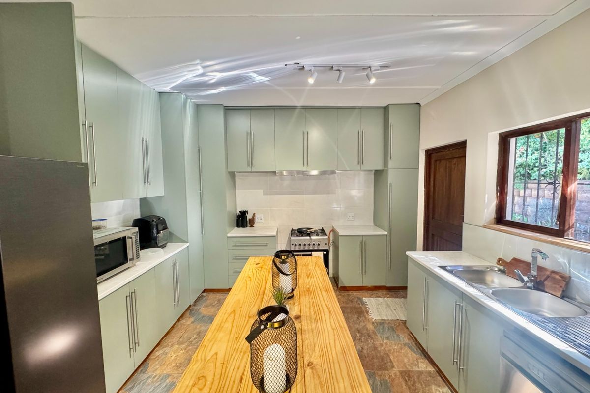 Modern kitchen featuring sage green cabinetry, stone countertops, a gas stove with extractor, and a central wooden island.