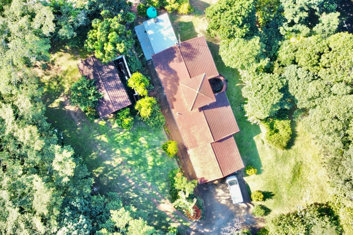Aerial view of the property showing the main dwelling with a tiled roof, secondary structure, water tank, and surrounding mature garden.