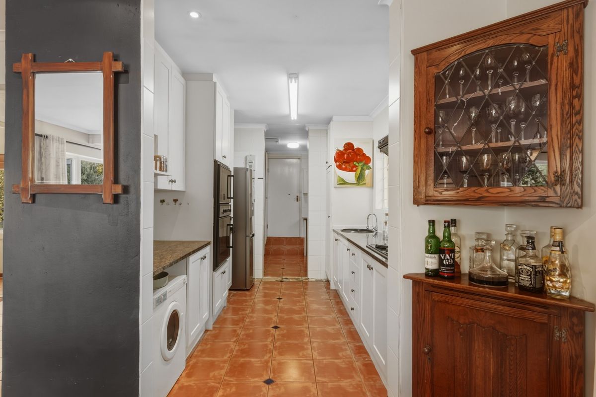 A functional galley-style kitchen featuring white cabinetry, integrated appliances, and tiled flooring, leading through to a secondary utility or laundry area.