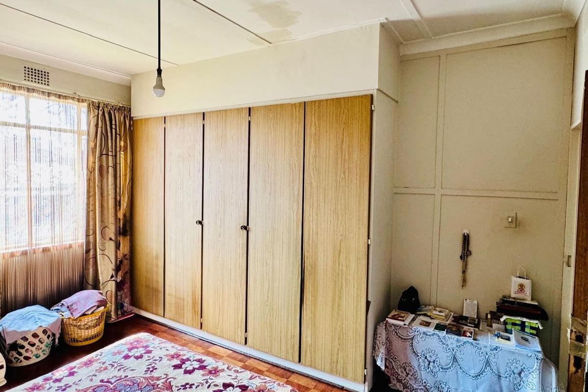A bedroom featuring parquet flooring and extensive built-in wooden cupboards, showing signs of ceiling water damage requiring attention.