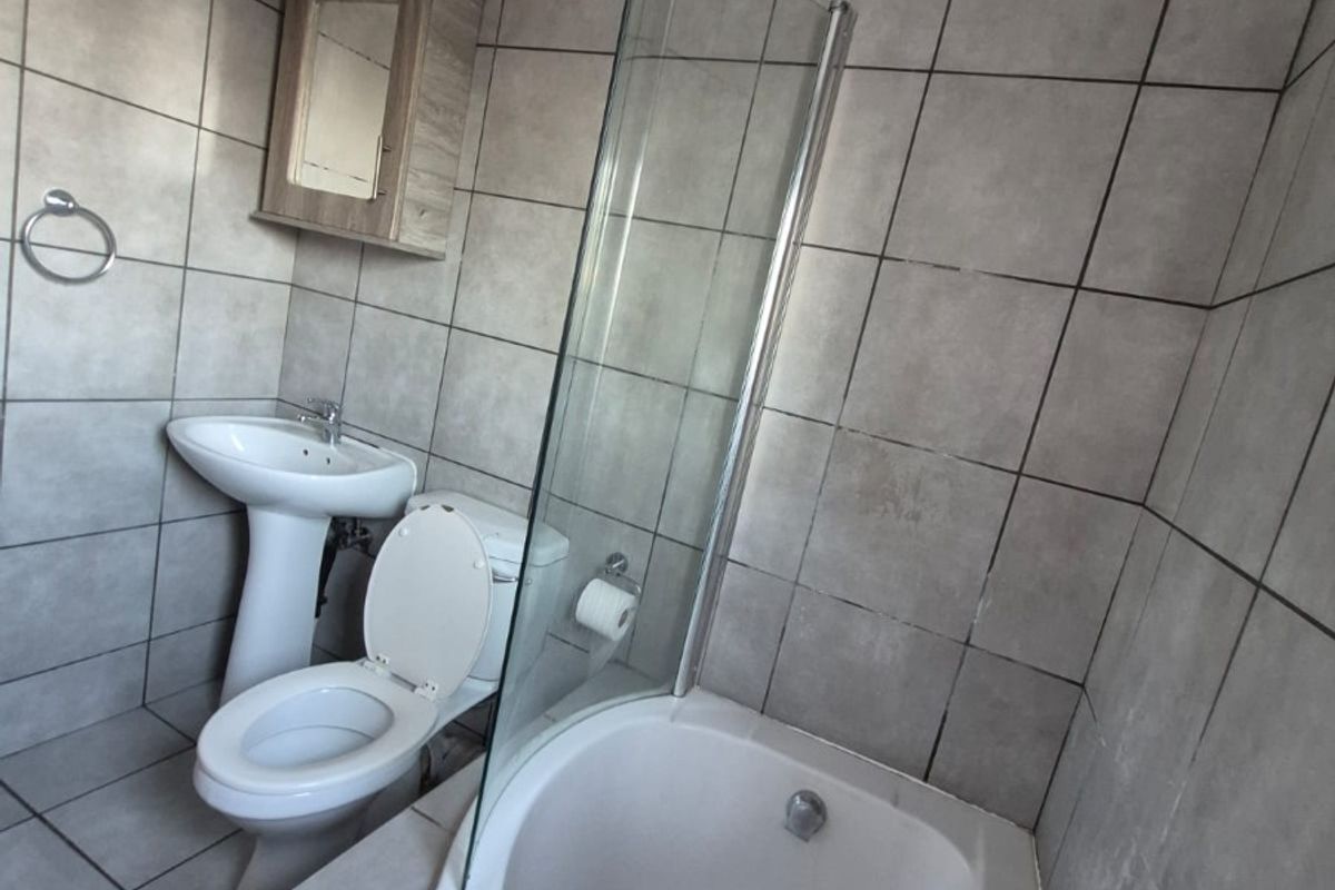 A functional bathroom featuring a combined shower and bathtub with a glass screen, pedestal basin, and toilet, finished with neutral wall and floor tiles.