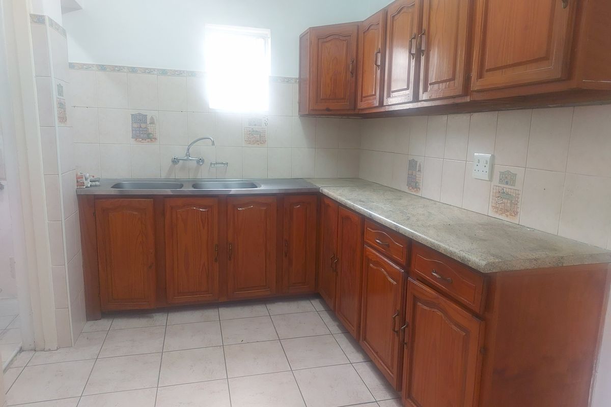 A functional kitchen featuring wooden cabinetry, laminate countertops, a double stainless steel sink, and tiled flooring.