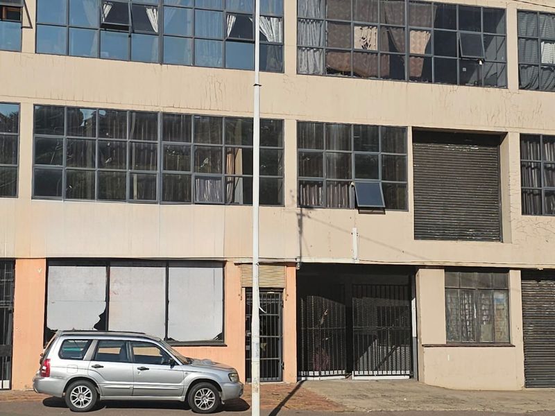 Multi-story industrial building facade featuring large grid windows, metal security gates, and roller shutter doors at street level.