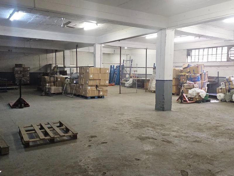 Spacious industrial warehouse area featuring concrete flooring, exposed structural support columns, and fluorescent overhead lighting, suitable for storage or manufacturing operations.